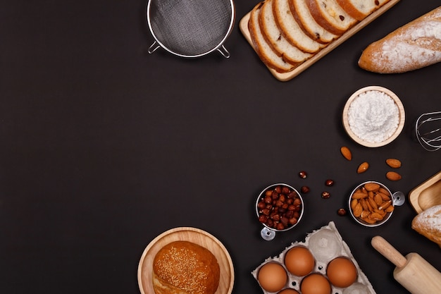 Homemade breads ingredients, flour, almond nuts, hazelnuts, eggs on dark background.