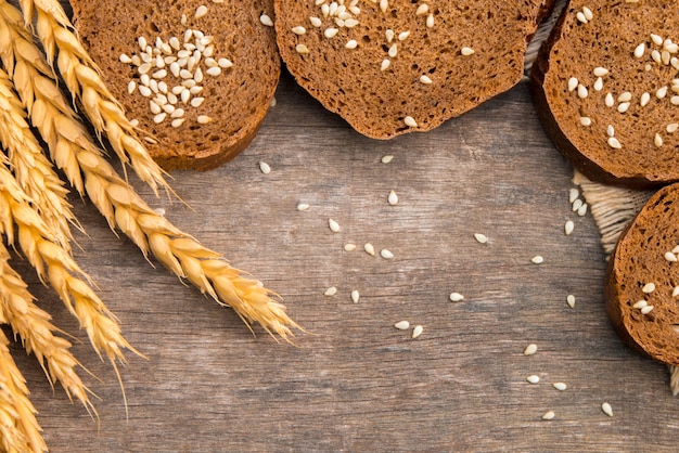 Homemade brown black on wooden background, black bread with rye spike and sesame, country still life top view