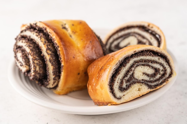 Homemade buns with poppy seeds on a white plate on a light background closeup selective focus