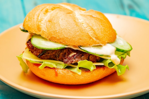 Homemade burger on a beige plate and on a turquoise wood background.