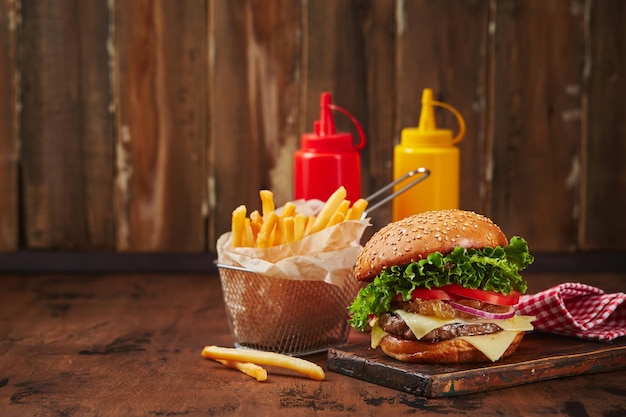 Homemade burger with beef cheese and onion marmalade on a wooden board fries in a metal basket and s...