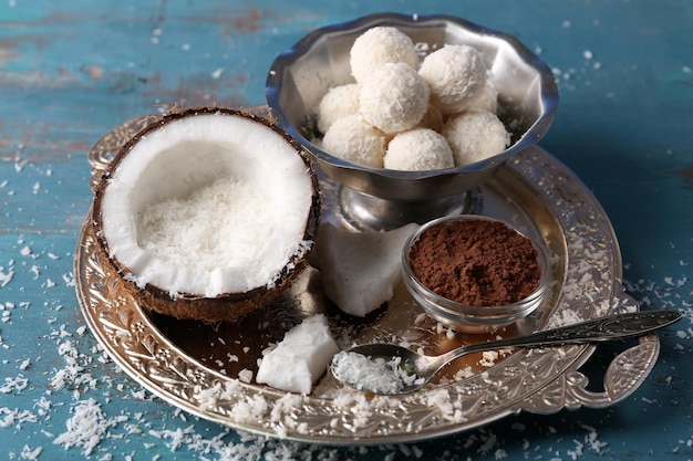 Homemade candies in coconut flakes and ingredients on color wooden background