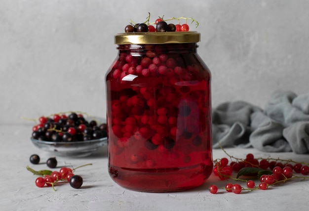 Homemade canned compote with black and red currants in glass jar on gray background