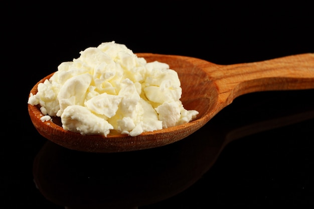 Homemade cheese in a spoon on a black surface close up