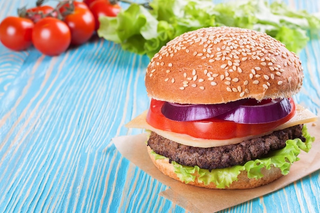 Homemade cheeseburger with beef patties and fresh salad on seasame buns, sered on blue wooden table.