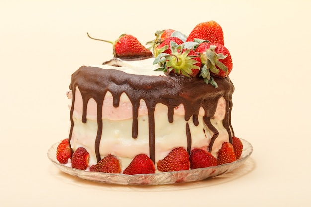 Homemade chocolate cake decorated with fresh strawberries and leaves of mint on glass plate on beige color background