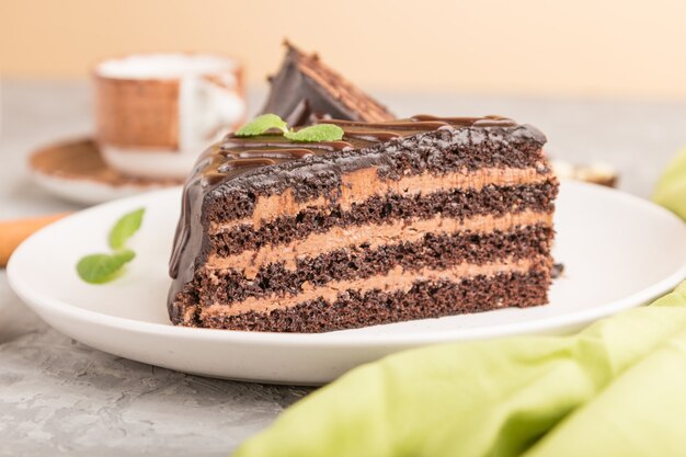 Homemade chocolate cake with milk cream and a cup of coffee on a gray concrete background. side view, selective focus.