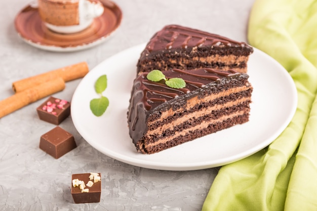 Homemade chocolate cake with milk cream and a cup of coffee on a gray concrete surface. side view, selective focus.