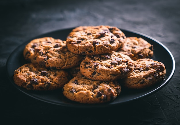 homemade chocolate chip cookies on a black plate on a dark table