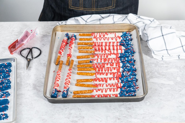 Homemade chocolate-covered pretzel rods decorated like the American flag drying on a baking sheet lined with parchment paper.