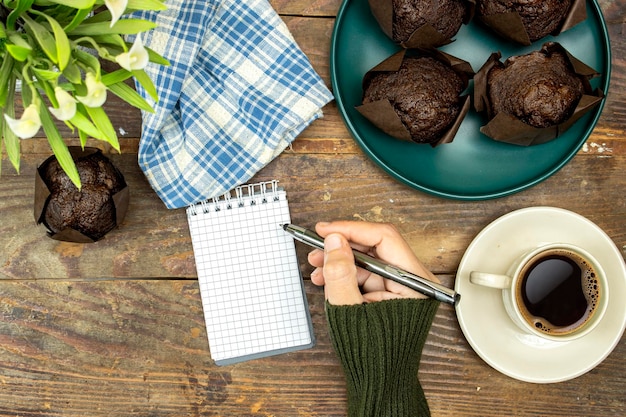 homemade chocolate muffins or madeleine in green plate with cup of coffee and pot of lilies flowers