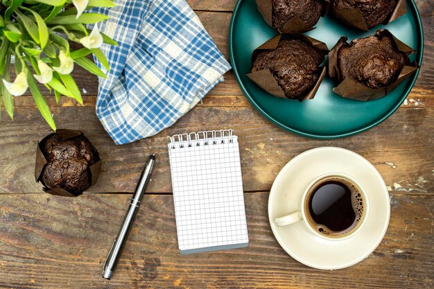 homemade chocolate muffins or madeleine in green plate with cup of coffee and pot of lilies flowers