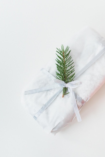 A homemade Christmas stollen sealed in white craft paper along with a sprig of a Christmas tree lies on a white background Gift wrap