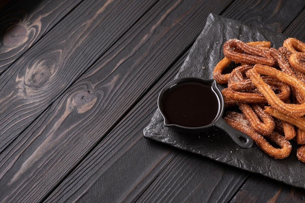 Homemade churros with chocolate on a dark wooden rustic background