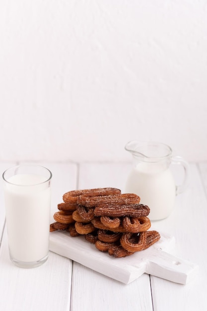 Homemade churros with milk and cream on a white wooden background