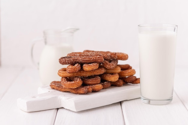 Homemade churros with milk and cream on a white wooden background