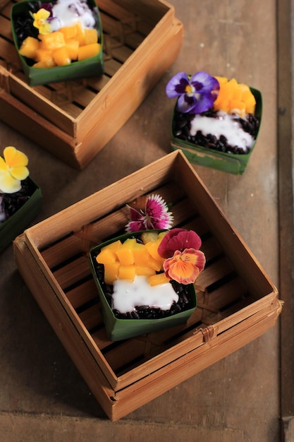 Homemade Coconut Black Sticky Rice with Mango in Pandan Leaves Cup, Selective Focus with Pansies Edibel Flower Topping