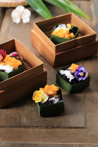 Homemade Coconut Black Sticky Rice with Mango in Pandan Leaves Cup, Selective Focus with Pansies Edibel Flower Topping