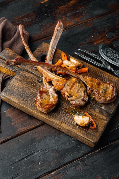 Homemade Cooked Lamb Chops with garlic and Carrots on wooden serving board on old dark wooden table background with copyspace and space for text