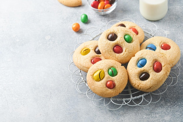 Homemade cookies with colorful chocolate candies and milk Stack of shortbread cookies with multi colored candy on plate with bottle of milk on light gray background Baby food concept Copy space