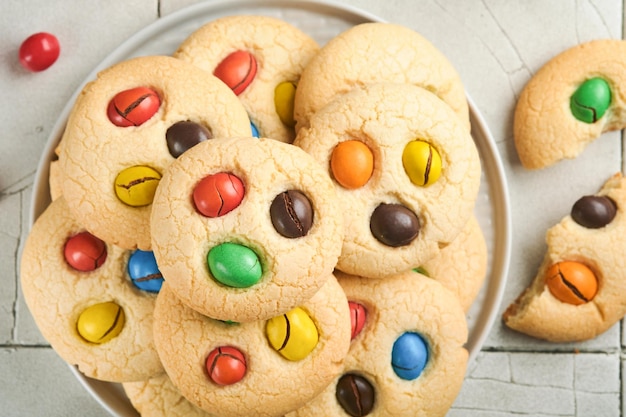 Homemade cookies with colorful chocolate candies and milk Stack of shortbread cookies with multi colored candy on plate with bottle of milk on light gray background Baby food concept Copy space