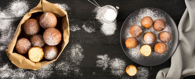 Homemade cottage cheese donuts in the paper package and plate on the black wooden background Top view Closeup