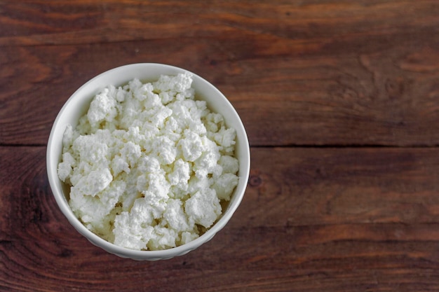 Homemade cottage cheese in a white bowl on a wooden background.