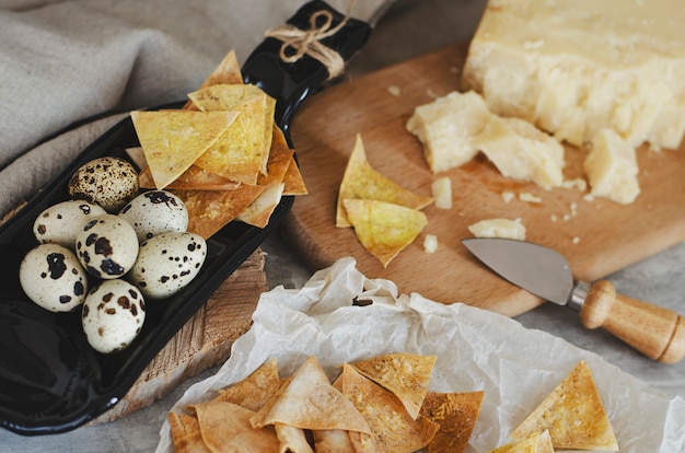 Homemade crispy chips from flatbread with parmesan cheese and quail eggs on serving plate made from bottle.