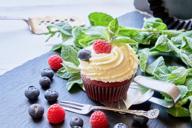 Homemade cupcake decorated with white cream and berries on black slate tray. Copy space