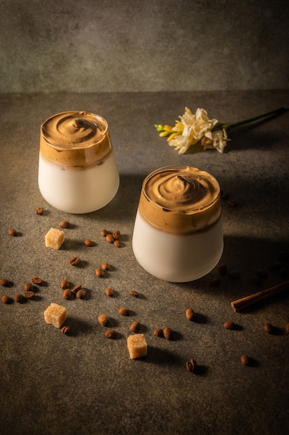 Photo homemade dalgona coffee on dark background next to coffee beans and cane sugar trendy fluffy creamy whipped drink made by instant coffee sugar and milk low key copy space