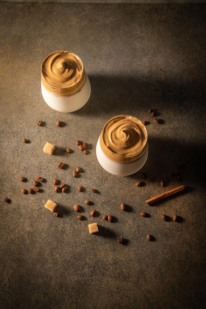 Homemade dalgona coffee on dark background next to coffee beans and cane sugar trendy fluffy creamy