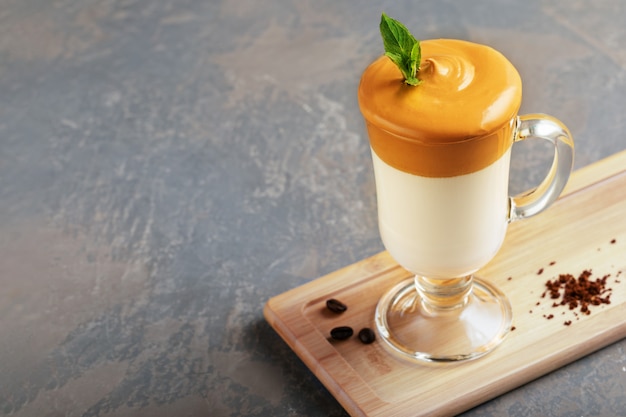 Homemade Dalgona coffee in glass cup on wooden board on grey background. Trend korean Iced  latte coffee drink with foam of instant coffee with coffee beans.