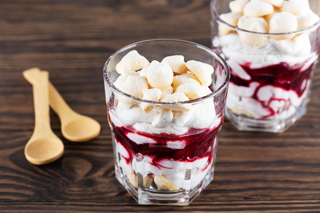 Homemade dessert with aquafaba meringue coconut cream and cherries in glasses on a wooden table