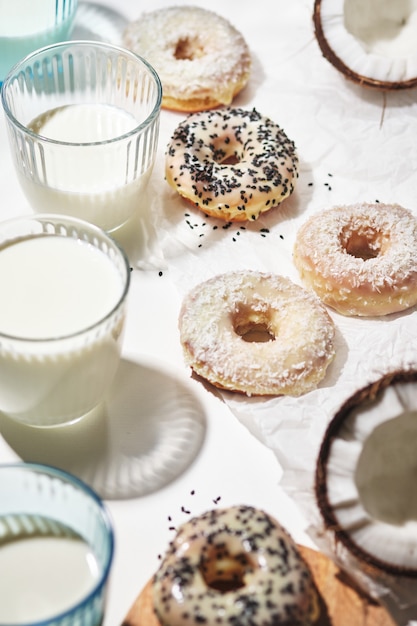 Homemade donuts with coconut and black sesame seeds in multi-colored glaze and glasses with milk