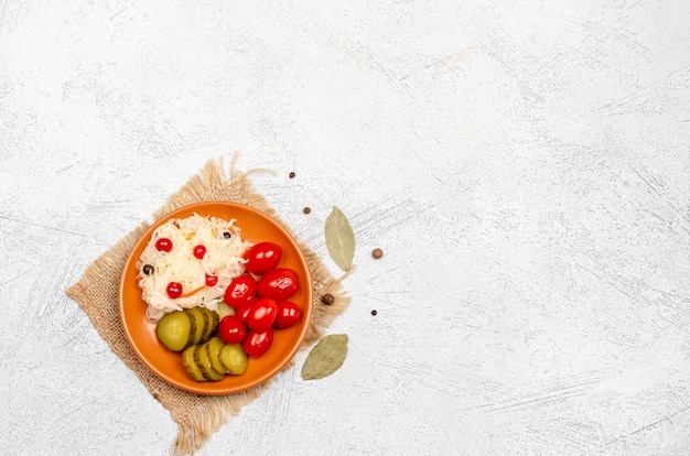 Homemade fermented products on a plate, sauerkraut, pickled tomatoes, pickles, light gray background.