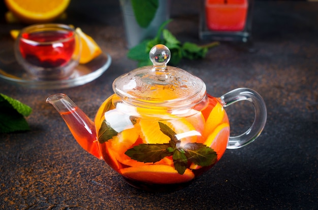 Homemade flavored Fruit Tea with orange and lemon Slice, berry, Mint and Honey in glass teapot on dark rustic background. Hot autumn or winter beverage. Process brewing tea,