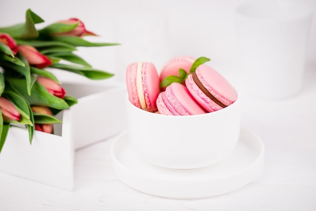 Homemade french dessert pink macaroons or macarons and spring tulips on white background, copy space