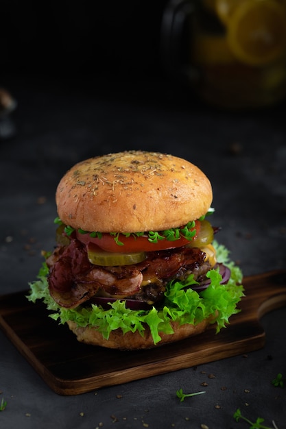 Homemade fresh beef burger on wooden board in dark mood photo style.