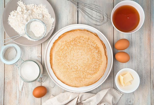 Homemade, fried pancakes on a plate and ingredients for cooking them on a light surface. Top view, with space for writing. The concept of cooking, recipes, Mardi Gras.