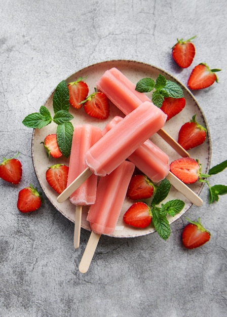 Homemade frozen strawberry ice cream popsicles and fresh strawberries on a concrete background