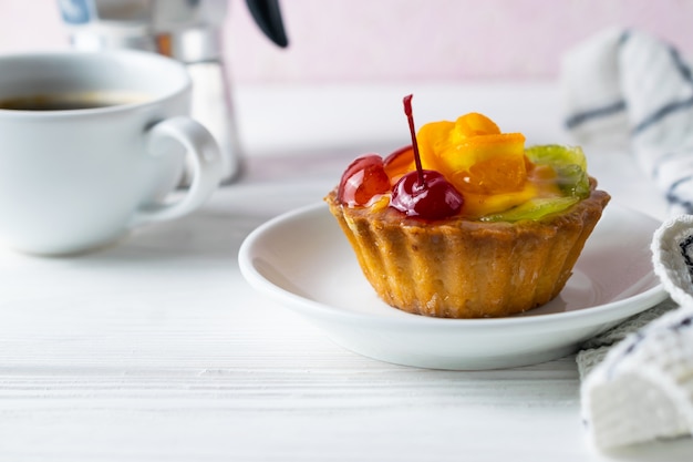 Homemade fruit tart with orange kiwi and cherry on white plate with black coffee