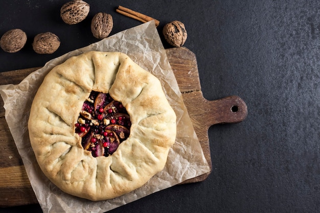 Homemade galette pie with apples, elder berries and walnuts decorated with fresh cowberry on dark