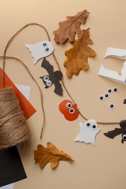 Homemade garland on a jute rope made of pumpkins, bats and ghosts with eyes on a beige background