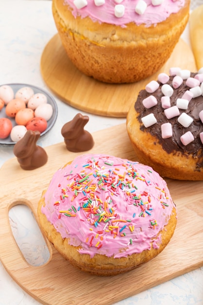 Homemade glazed and decorated easter pies with chocolate eggs and rabbits on a white concrete background and yellow textile. Side view, close up.