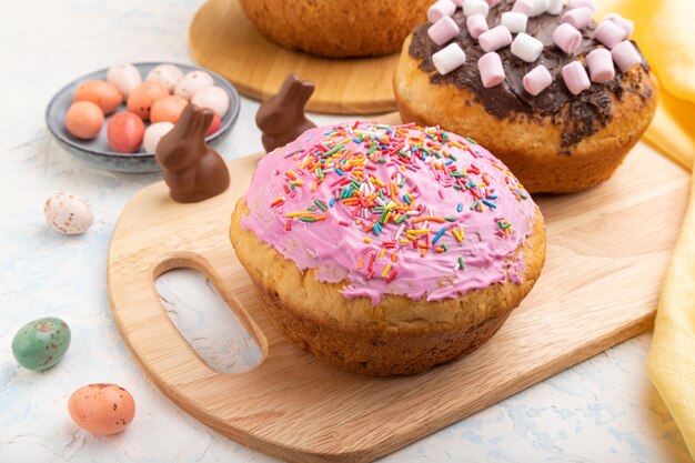 Homemade glazed and decorated easter pies with chocolate eggs and rabbits on a white concrete background and yellow textile.