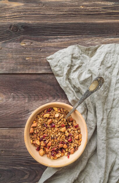 Photo homemade granola, muesli with nuts and dried cranberries in wooden bowl on rustic wooden table. top view.