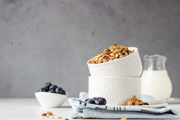 Homemade granola in a white ceramic bowl with raisins, blueberries and milk. Healthy breakfast ingredients