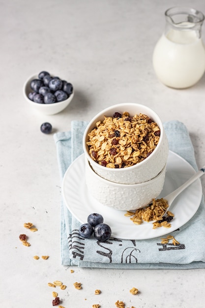 Homemade granola in a white ceramic bowl with raisins, blueberries and milk. Healthy breakfast ingredients