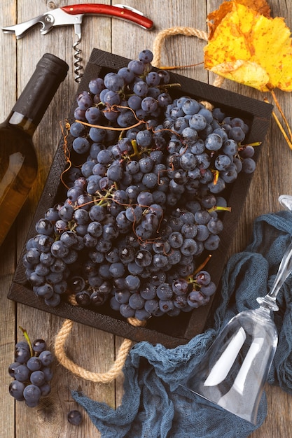 Homemade grapes in a black box, a bottle of wine and corkscrew on old wooden background. Vintage style. Toned image.Top view