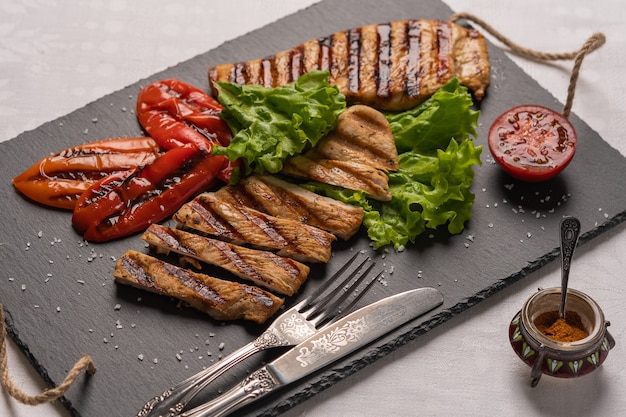 Homemade grilled turkey breast steaks with baked pepperslettuce and tomato on a black board with